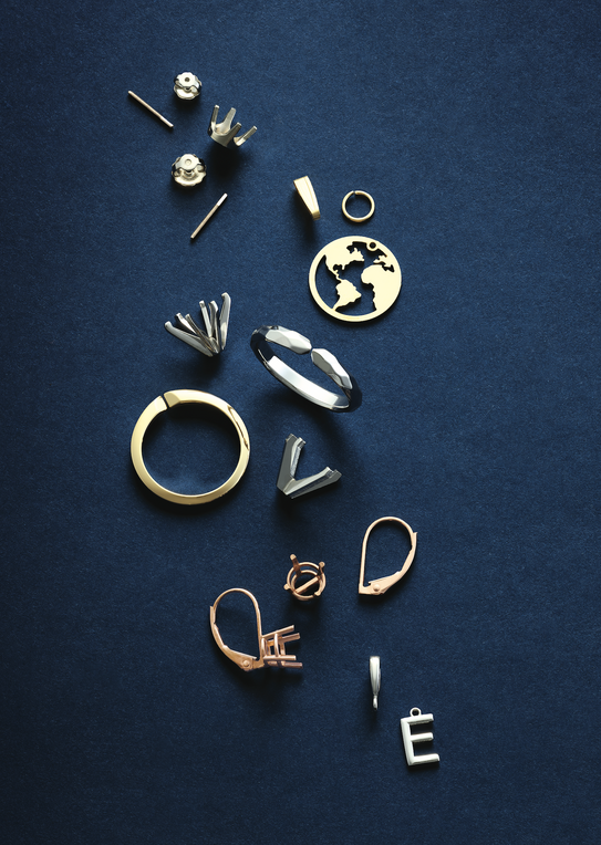 gold and silver jewelry components, including rings, earring backs, and a world tree pendant, laid out on a dark background. These pieces showcase the craftsmanship and detail that First Person Jewelers puts into their custom-made jewelry designs.