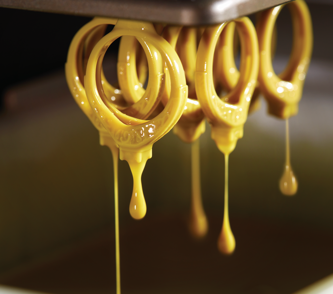 Gold rings being dipped in a liquid coating as part of the jewelry-making process. This image showcases the meticulous craftsmanship and attention to detail in creating high-quality pieces at First Person Jewelers.