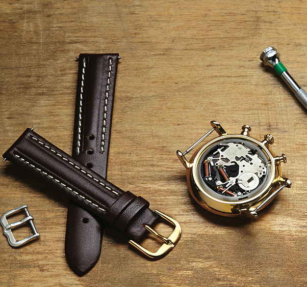 Disassembled luxury watch with leather straps and tools laid out on a wooden surface. This image highlights the intricate craftsmanship and repair services provided by First Person Jewelers for high-end timepieces