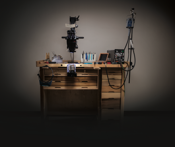 Jewelry maker's workbench with specialized tools, including a microscope and precision instruments, set against a dark background. This setup highlights the meticulous craftsmanship and attention to detail at First Person Jewelers