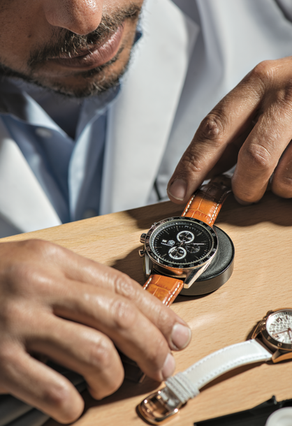 Jeweler inspecting a luxury watch with a leather strap at a workbench. This image showcases the expert craftsmanship and attention to detail offered by First Person Jewelers in their high-quality timepiece services.